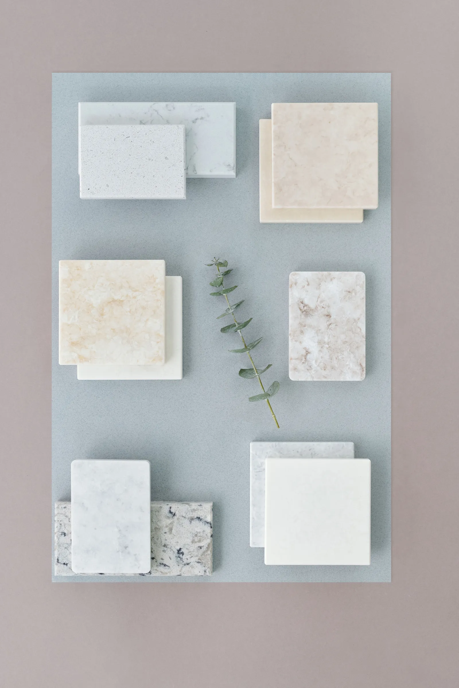 Stock photo: countertop material samples in white, grey and cream laid out on a blue-grey board with a sprig of eucalyptus